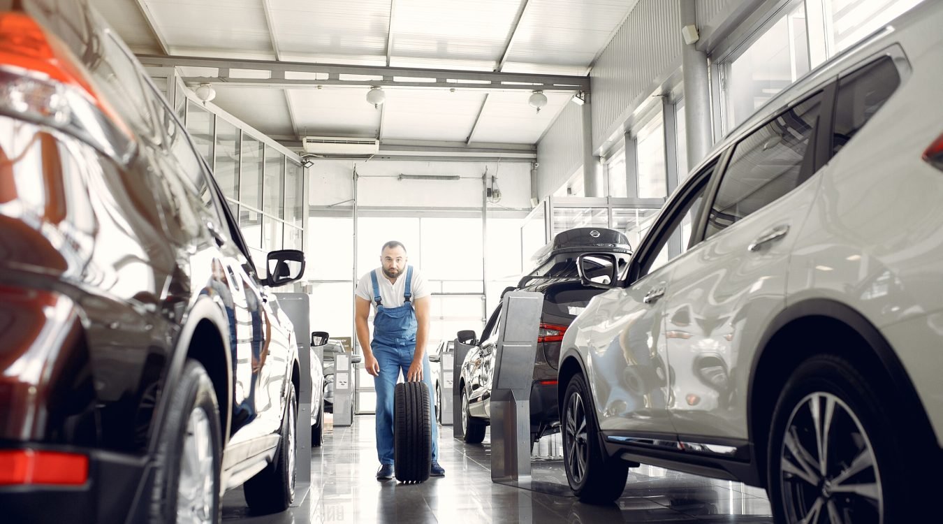 Wrker in a car salon. Expert checks the car. Man in a blue uniform.